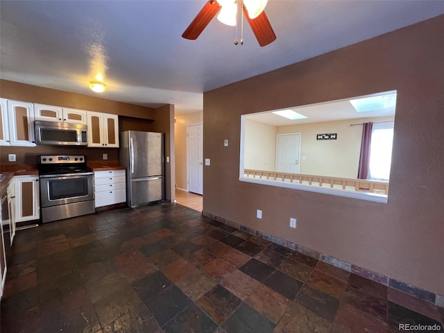 kitchen featuring appliances with stainless steel finishes, dark tile floors, white cabinetry, and a skylight