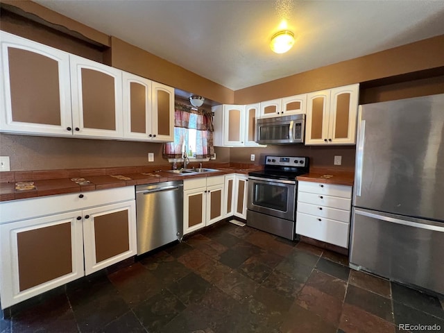 kitchen featuring appliances with stainless steel finishes, sink, white cabinetry, and dark tile flooring