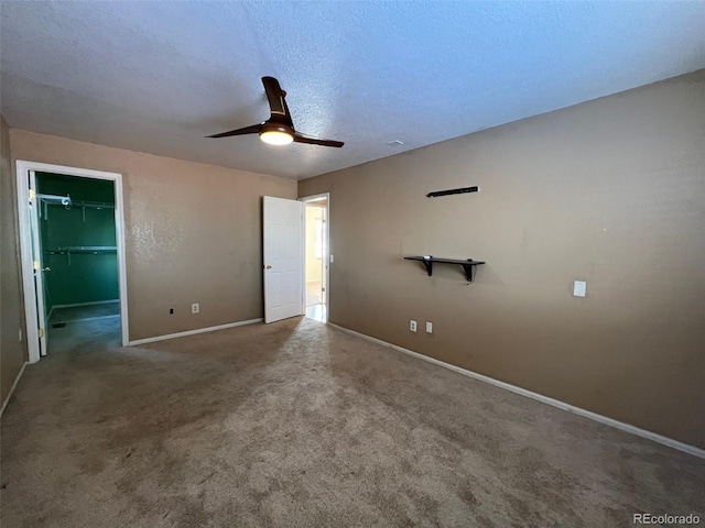 unfurnished bedroom with dark carpet, ceiling fan, a closet, a textured ceiling, and a spacious closet