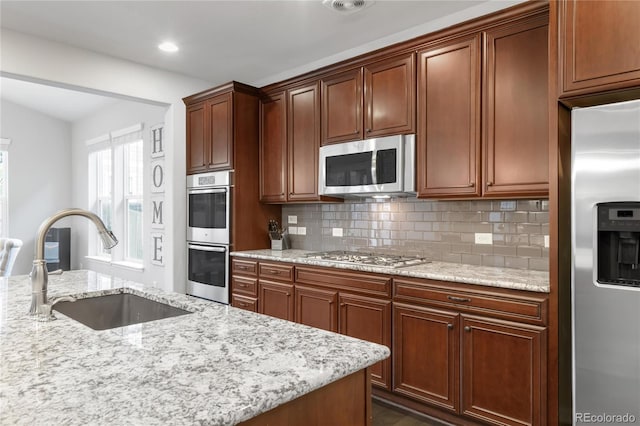 kitchen with tasteful backsplash, a sink, light stone counters, stainless steel appliances, and recessed lighting