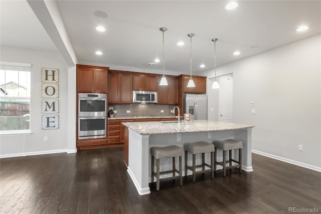 kitchen featuring decorative backsplash, a kitchen island with sink, dark wood-type flooring, a sink, and stainless steel appliances