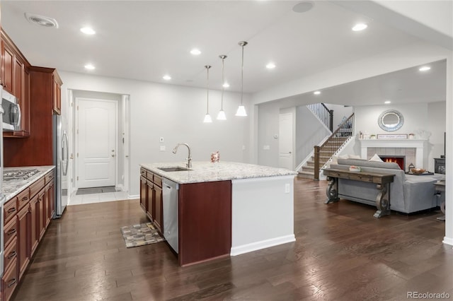 kitchen featuring light stone countertops, appliances with stainless steel finishes, a sink, an island with sink, and dark wood-style floors