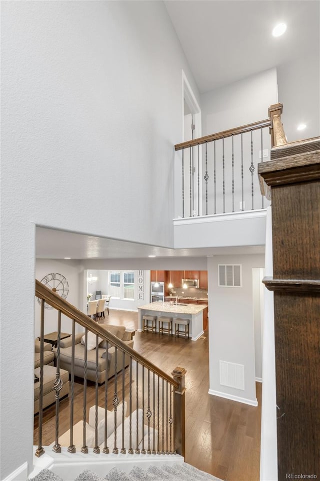 stairway featuring visible vents, recessed lighting, a towering ceiling, and wood finished floors