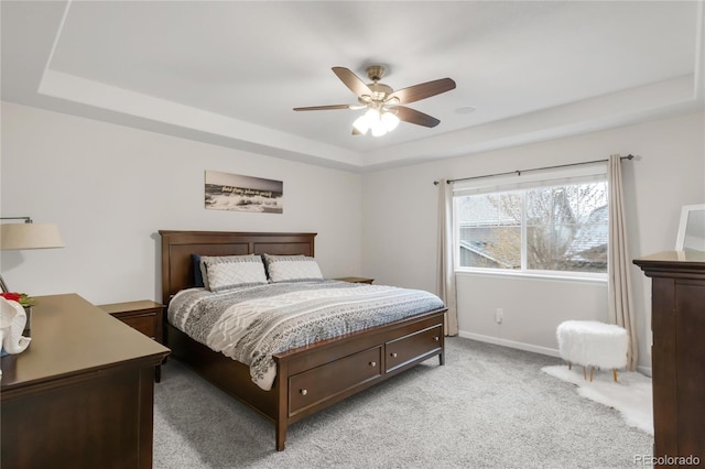bedroom with a raised ceiling, baseboards, light carpet, and a ceiling fan