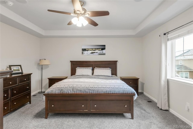 bedroom featuring light colored carpet, baseboards, and a tray ceiling