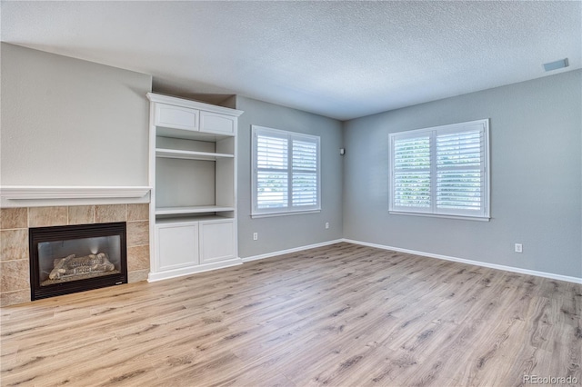 unfurnished living room featuring visible vents, a tiled fireplace, light wood-style floors, a textured ceiling, and baseboards