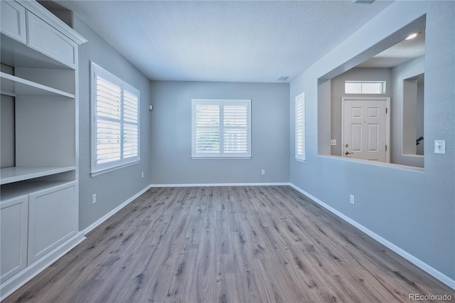 unfurnished living room featuring a textured ceiling, wood finished floors, visible vents, and baseboards