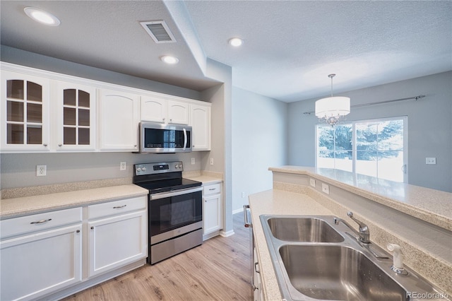 kitchen with white cabinets, glass insert cabinets, appliances with stainless steel finishes, light wood-style floors, and a sink