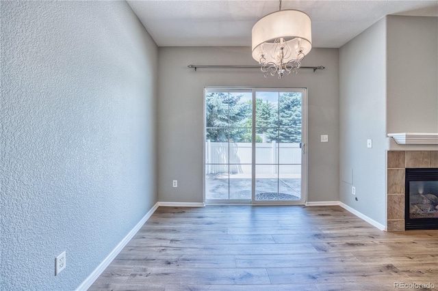 interior space with baseboards, a tiled fireplace, wood finished floors, and an inviting chandelier