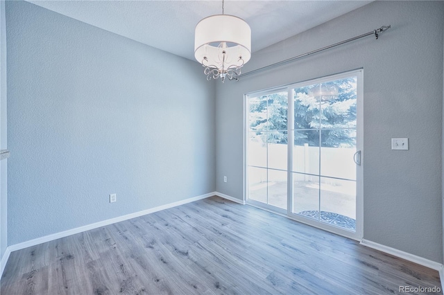 spare room with a chandelier, baseboards, and wood finished floors