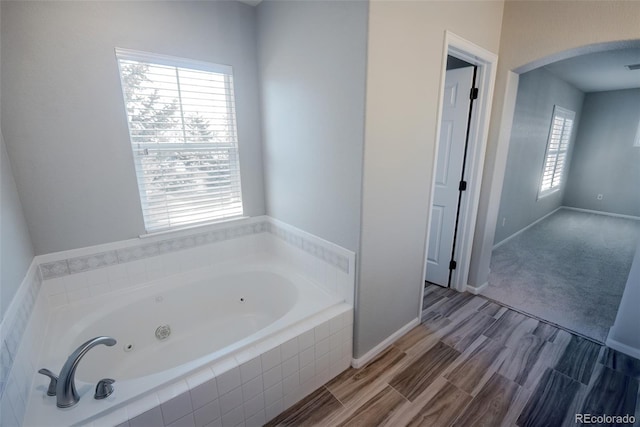 full bathroom with a jetted tub, baseboards, and wood finished floors