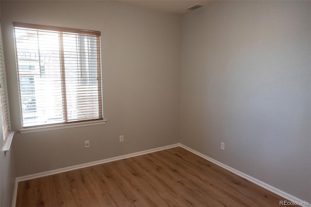 spare room with baseboards, visible vents, and wood finished floors