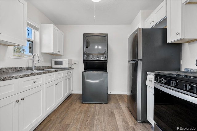 kitchen featuring white microwave, stacked washer / dryer, white cabinets, light wood-style floors, and black range with gas stovetop