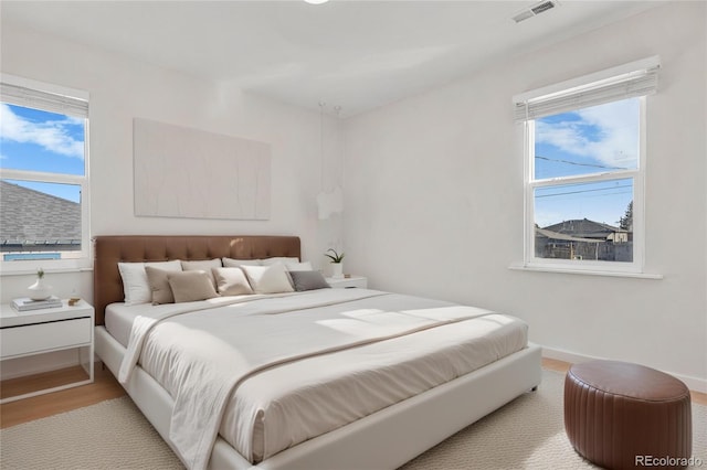 bedroom with baseboards, visible vents, and wood finished floors