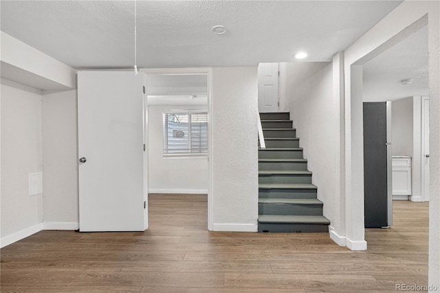 stairway with a textured ceiling, baseboards, and wood finished floors