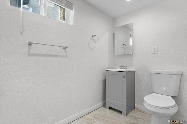 half bath featuring a textured wall, toilet, wood finished floors, vanity, and baseboards