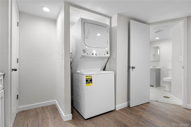 clothes washing area featuring stacked washer and dryer, light wood-style flooring, laundry area, and baseboards