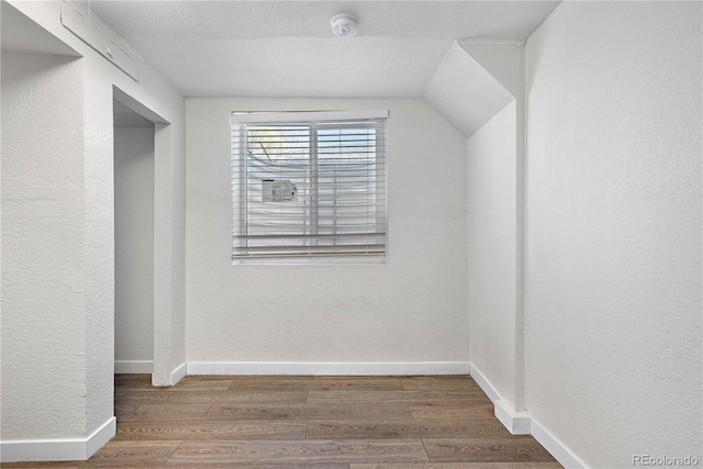 additional living space with lofted ceiling, a textured wall, baseboards, and wood finished floors