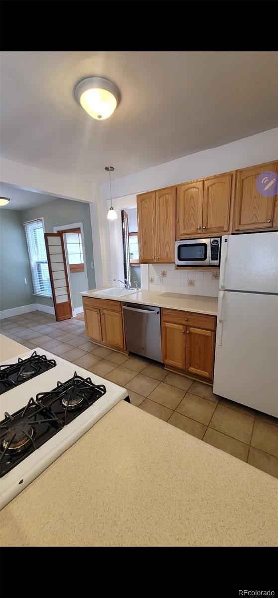 914 E Iowa Ave, Denver, CO 80210 - kitchen with stainless steel appliances, light tile patterned floors, light countertops, and brown cabinets
