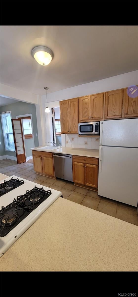 914 E Iowa Ave, Denver, CO 80210 - kitchen with appliances with stainless steel finishes, light tile patterned flooring, light countertops, brown cabinets, and pendant lighting