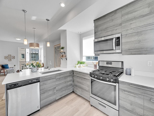 kitchen featuring gray cabinets, a sink, appliances with stainless steel finishes, a peninsula, and light countertops