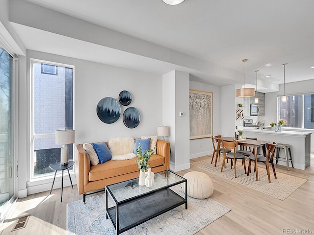 living area featuring light wood-type flooring, baseboards, visible vents, and a healthy amount of sunlight