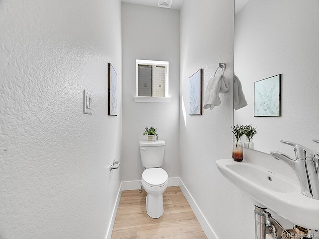 bathroom featuring baseboards, toilet, wood finished floors, a textured wall, and a sink