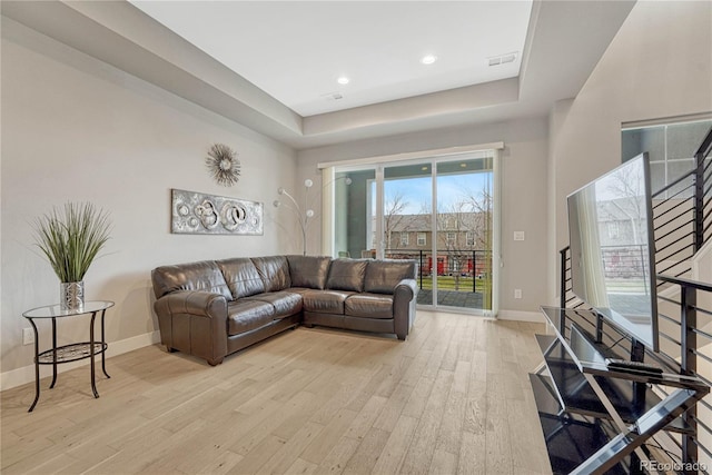 living room with stairs, light wood-style floors, visible vents, and baseboards