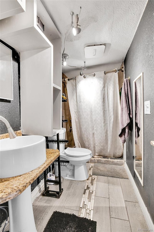 8430 Madison Way, Denver, CO 80229 - bathroom with a textured wall, a stall shower, toilet, a textured ceiling, and a sink
