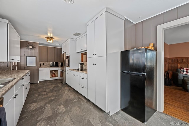 kitchen featuring black refrigerator, tasteful backsplash, white cabinets, sink, and light stone counters