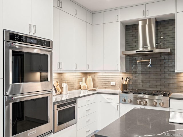 kitchen with white cabinets, stainless steel appliances, wall chimney exhaust hood, and stone counters