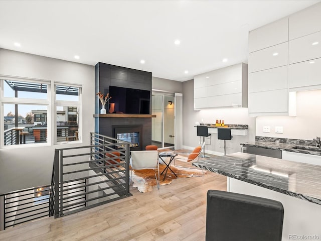 kitchen featuring sink, dark stone countertops, a fireplace, white cabinets, and light wood-type flooring