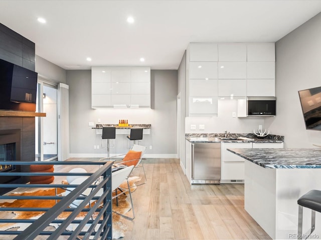 kitchen with a tiled fireplace, sink, white cabinets, and light hardwood / wood-style floors