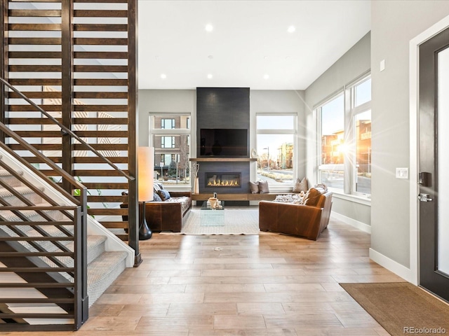 living area featuring a large fireplace, baseboards, stairway, light wood-type flooring, and recessed lighting