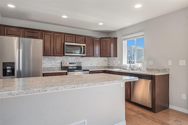 kitchen with light wood-type flooring, tasteful backsplash, dark brown cabinets, stainless steel appliances, and sink