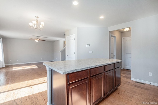 kitchen featuring ceiling fan with notable chandelier, a kitchen island, light wood-type flooring, and decorative light fixtures