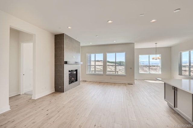 unfurnished living room with a tile fireplace, light hardwood / wood-style floors, and an inviting chandelier