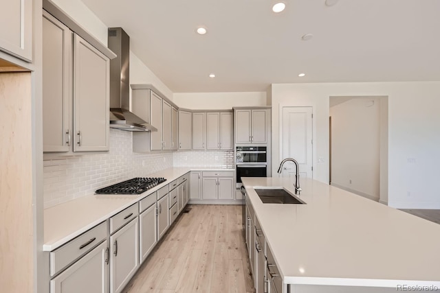 kitchen featuring gray cabinetry, wall chimney exhaust hood, light hardwood / wood-style flooring, double oven, and sink