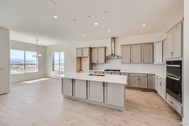 kitchen featuring light hardwood / wood-style floors, a center island with sink, wall chimney exhaust hood, and sink