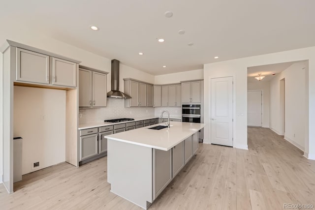 kitchen with light hardwood / wood-style floors, sink, an island with sink, gas cooktop, and wall chimney exhaust hood