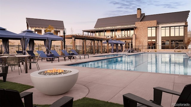 pool at dusk with a gazebo, a patio area, and an outdoor fire pit