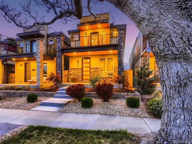 contemporary home with stucco siding, stone siding, and a balcony