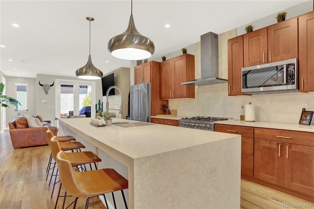 kitchen with decorative backsplash, light wood-style floors, appliances with stainless steel finishes, and wall chimney range hood