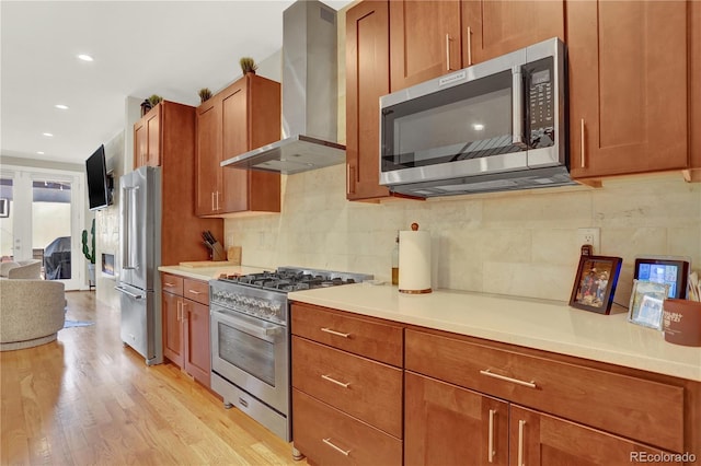 kitchen with ventilation hood, premium appliances, light wood-style flooring, decorative backsplash, and brown cabinetry