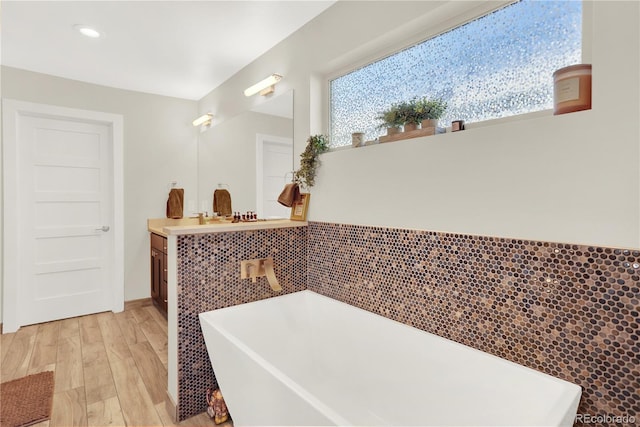 bathroom with a soaking tub, plenty of natural light, vanity, and wood finished floors