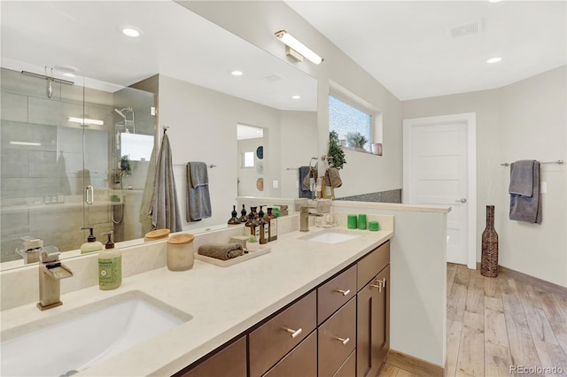 full bath featuring a sink, double vanity, wood finished floors, and a shower stall