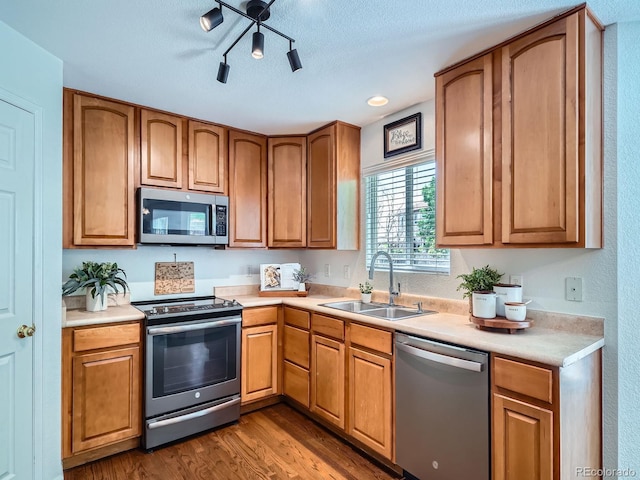 kitchen featuring stainless steel appliances, a sink, dark wood-style flooring, light countertops, and brown cabinetry
