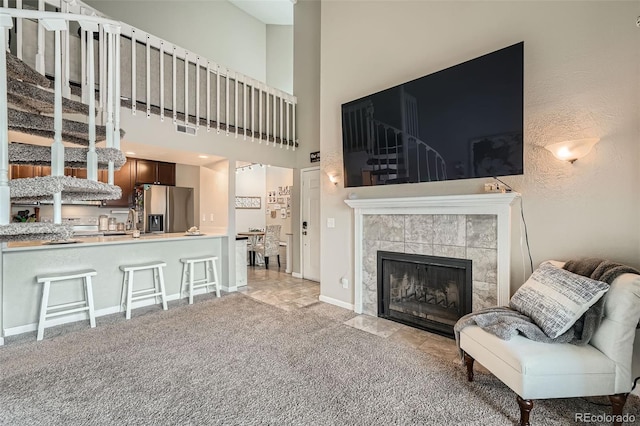 10872 W Evans Ave Unit 3D, Lakewood, CO 80227 - living area featuring a tile fireplace, a towering ceiling, light colored carpet, stairs, and baseboards