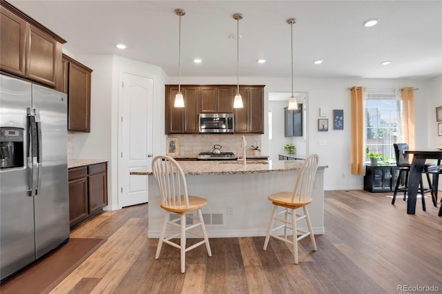 kitchen with stainless steel appliances, wood finished floors, backsplash, a breakfast bar area, and a sink