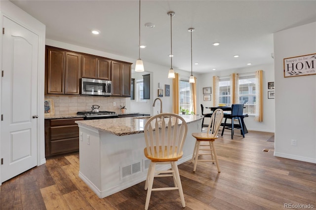 kitchen with stainless steel appliances, dark wood-style floors, decorative backsplash, light stone countertops, and recessed lighting